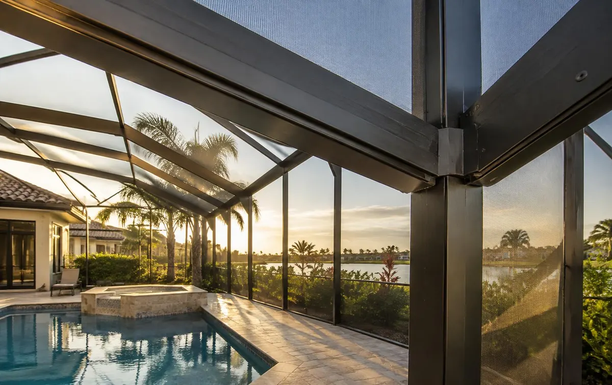 Corner of a dark aluminum pool enclosure frame with screen panels above a pool deck